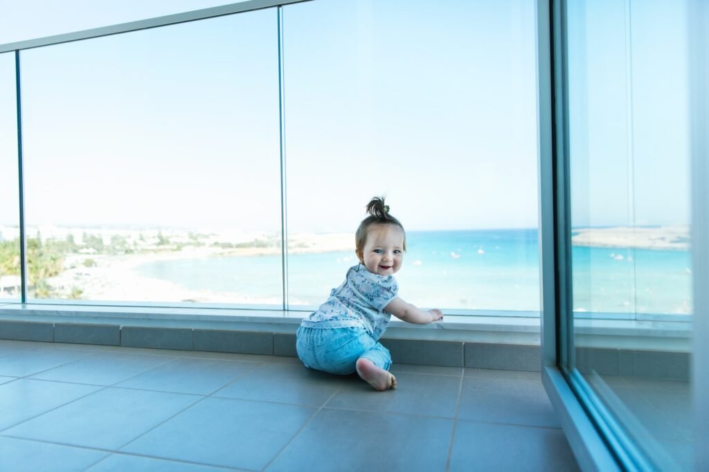 Toddler happy girl looking out at Cyprus, Mediterranean Sea from a glass balcony